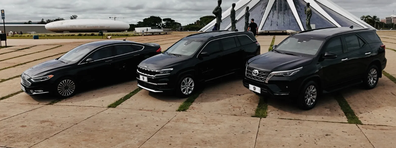 Sedan, van e SUV da frota BSB Explore em frente à Catedral Metropolitana de Brasília